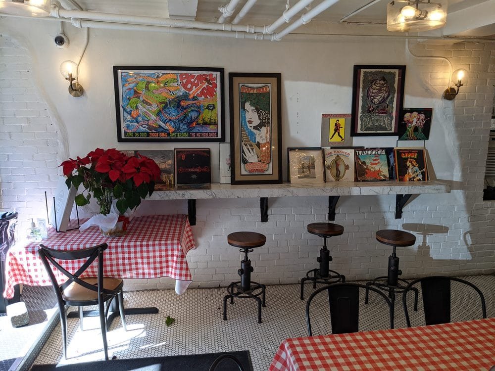 Inside Grigg Street Pizza — white tiled walls, concert posters including Pearl Jam, marble counter, and red checkered tablecloths